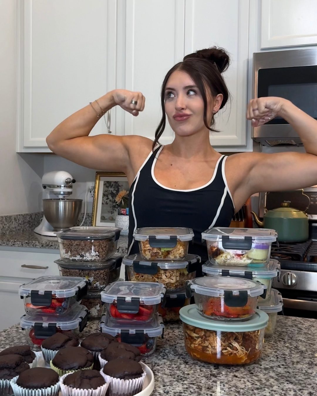 Brooke flexing behind a counter full of her weekly meal prep containers